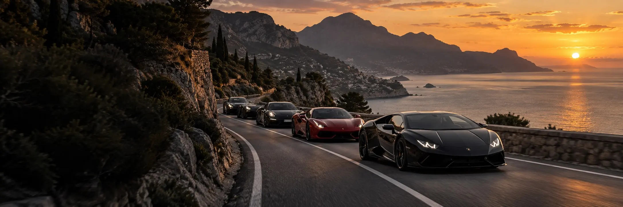 A group of sports cars driving together along a coastal mountain road.